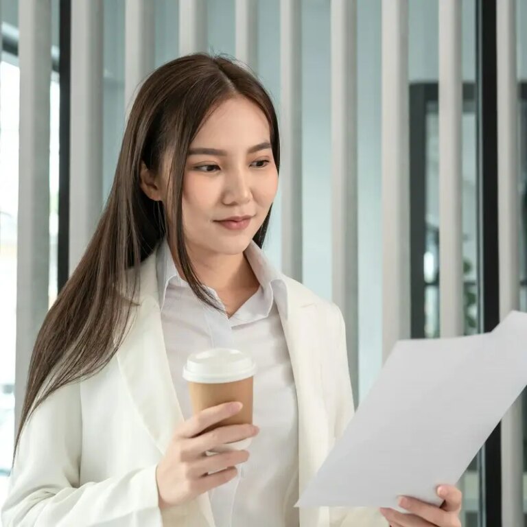 Asian businesswoman analyzing documents (data graph) and sipping coffee while working in a office