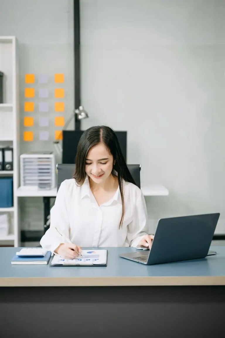 Asian Businesswoman Analyzing Finance on Tablet and Laptop at modern Office Desk tax