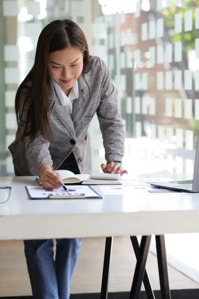 Business woman working on financial report by calculator and laptop on desk in office.