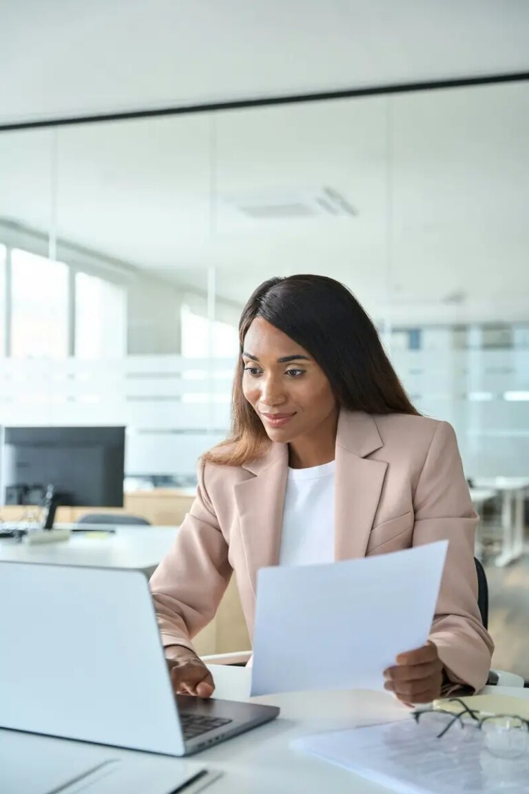 Female account manager checking document using laptop in office, vertical.