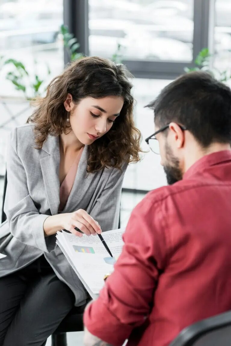 selective focus of account manager pointing at papers and talking with colleague