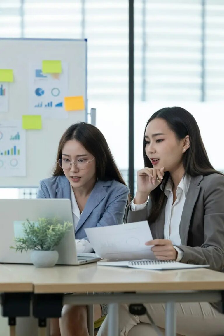 Two Female Accountant Collaborating on Financial Reports in a Modern Office Setting with Charts and